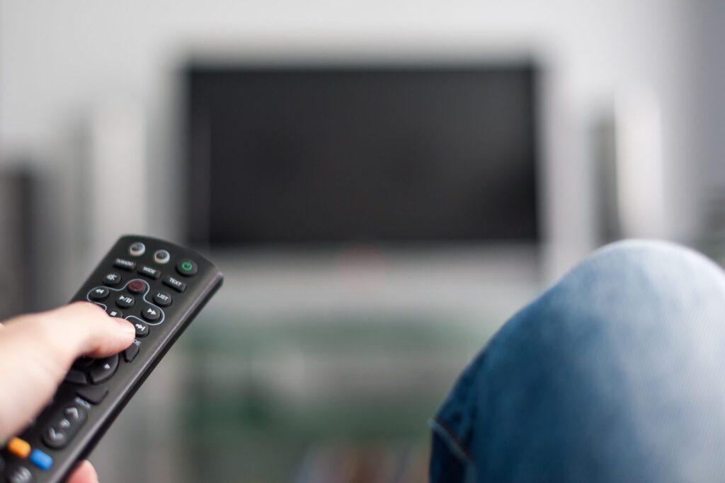 Person holding a television remote control with a TV in the background.