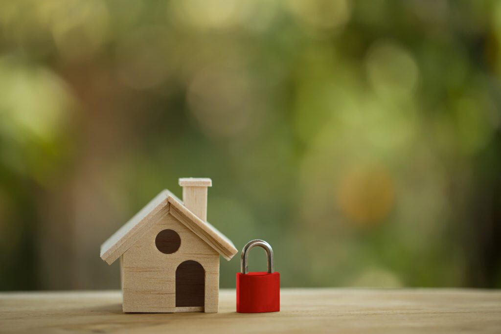 Wooden model of a home next to a lock on a wooden surface.