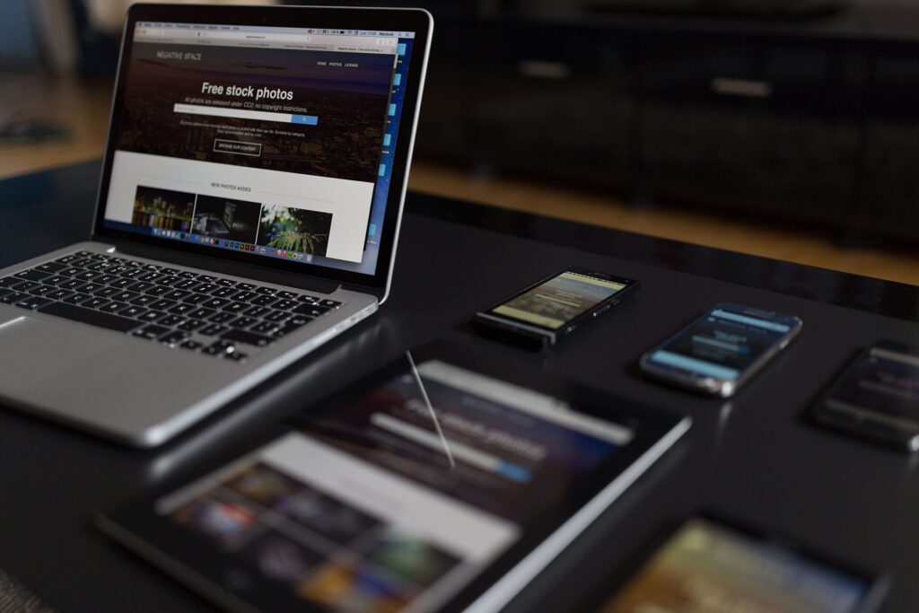 A series of electronic devices on a desk, including a laptop, phones, and tablets.