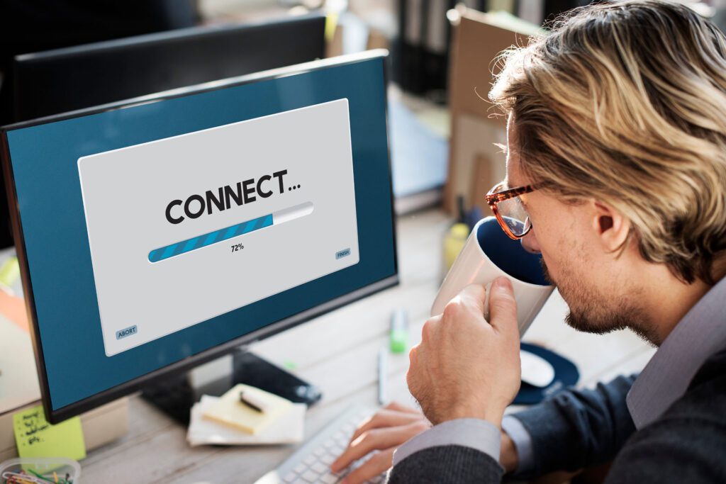 Man with glasses and holding a cup of coffee in his hands using a computer with the word “connect” on the screen with a loading bar.