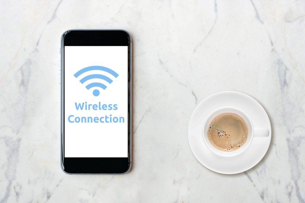 Cell phone with the words “wireless connection” on the screen with a Wi-Fi logo next to a cup of coffee on a marble surface.