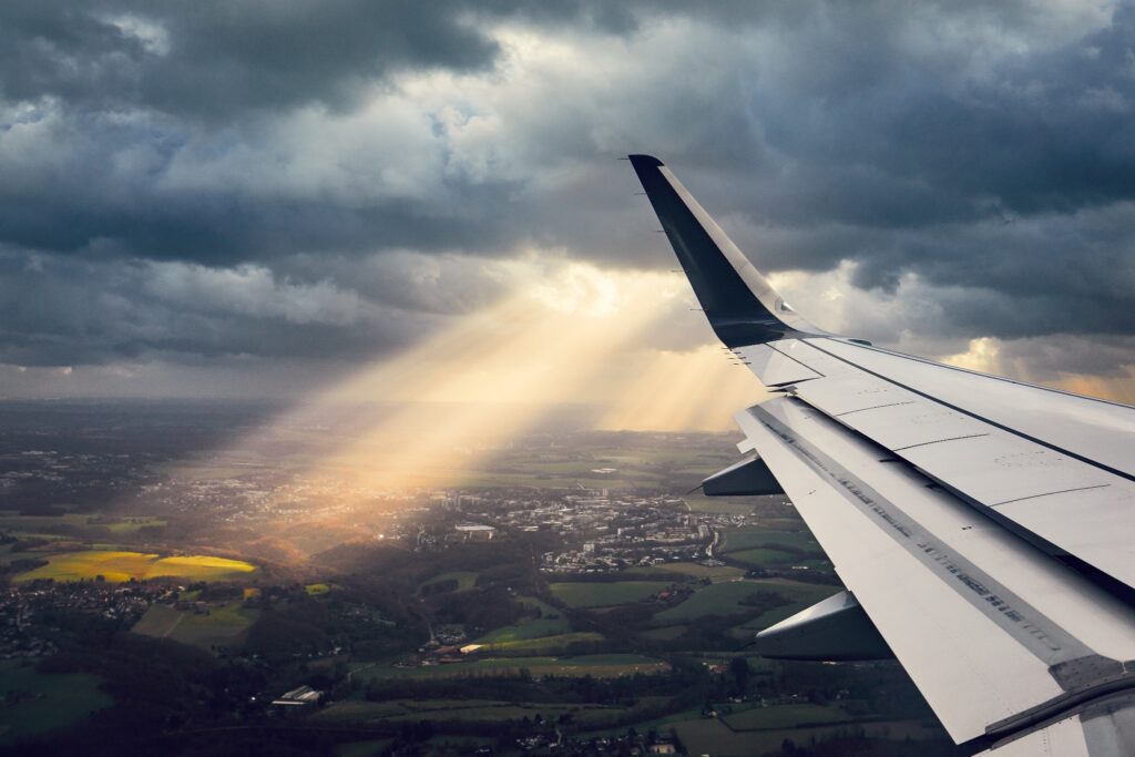 A view of a plane’s wing as it travels through a cloudy area, lit up by a sunbeam.