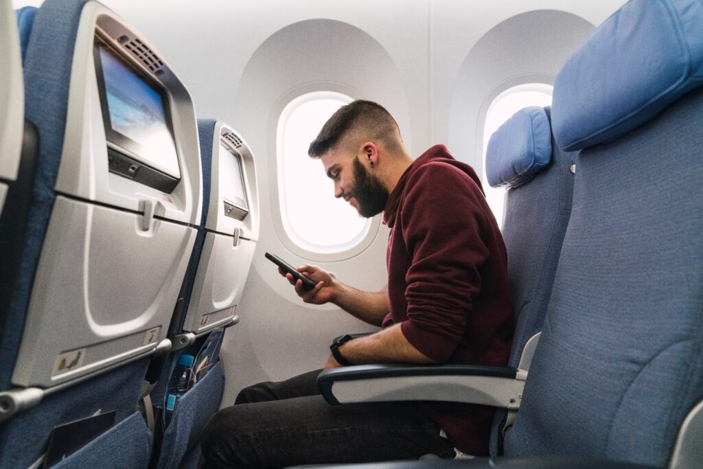 A bearded man using a phone while inside a plane. 