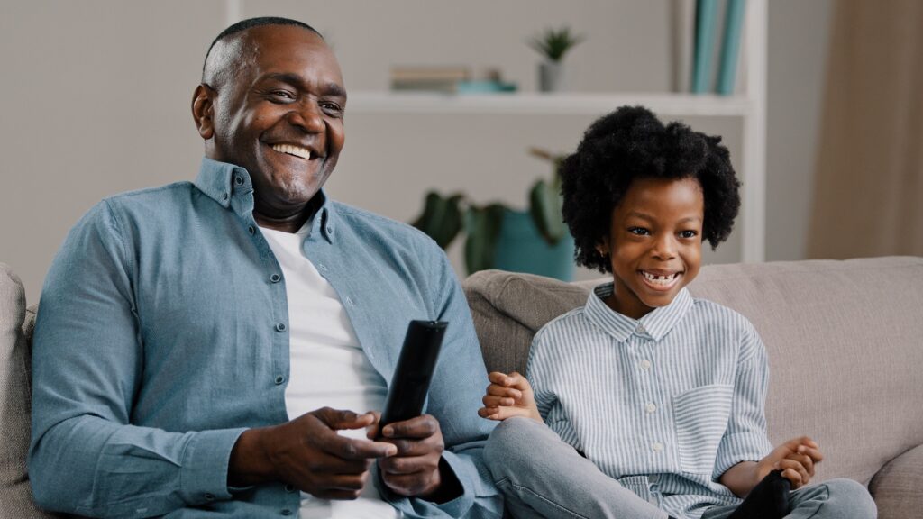 A father and daughter watch TV while sitting on a couch.