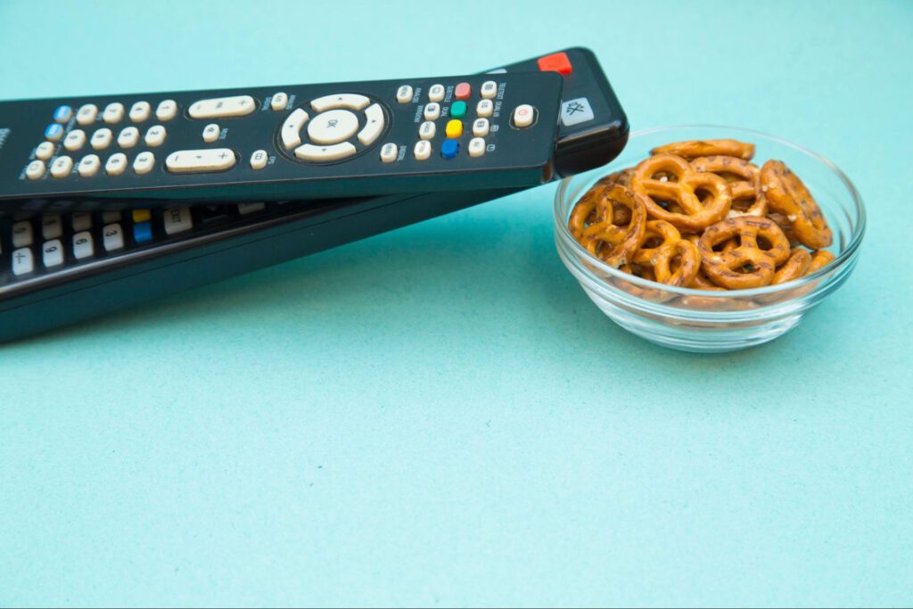 Two remotes and a bowl of pretzels against a light blue background.