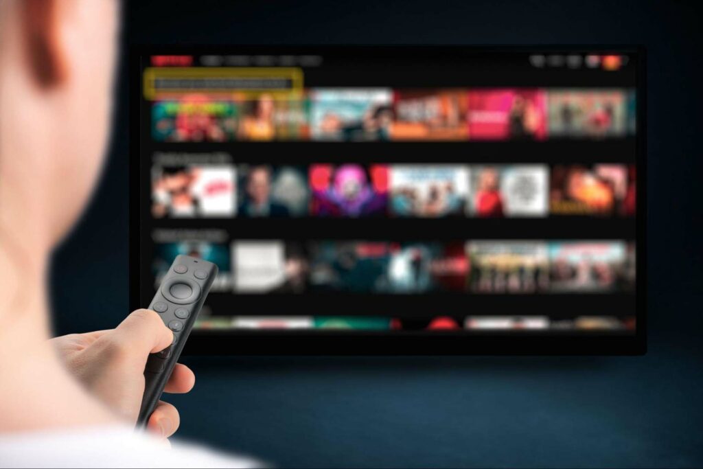 Woman holding a remote while looking at various shows and movies on a streaming service.