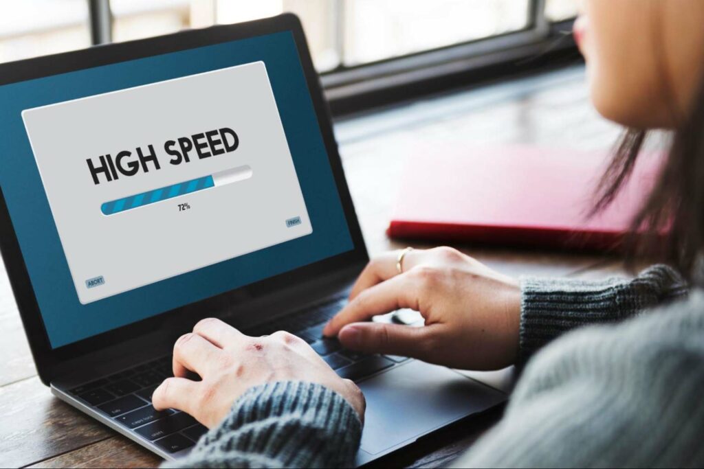 Woman typing on a laptop with the words “high speed” on the screen with a loading bar underneath at 72%.