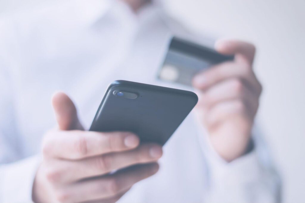 Man holding a cell phone in one hand and a credit card in the other.