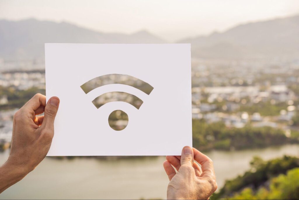 A pair of hands holding up a sign with the Wi-Fi symbol in front of a view of a city.