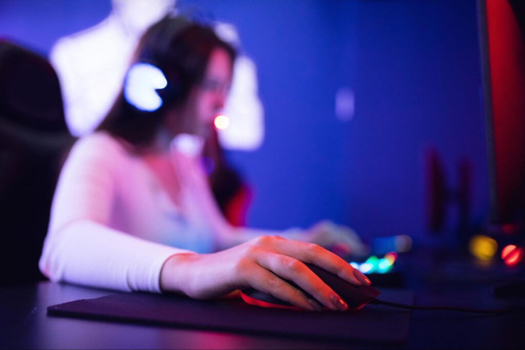 A blurred view of a woman playing video games at a computer with neon lighting.