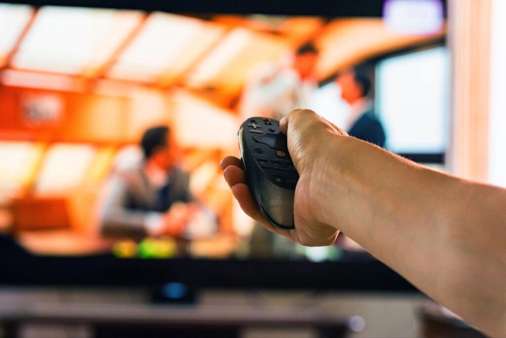 A person holds a remote, pointing it at a TV.
