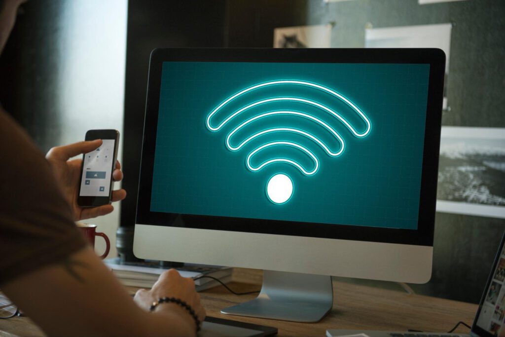 A person uses a computer and a phone. The desktop computer has a screen that reads “Wi-Fi.”