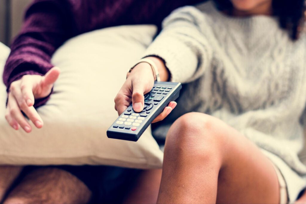 A couple sits on a sofa holding a TV remote.