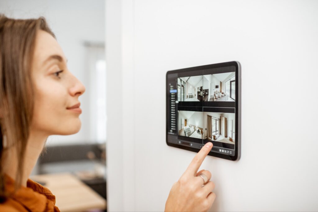 A woman controls her home security camera by using a tablet mounted on her wall.