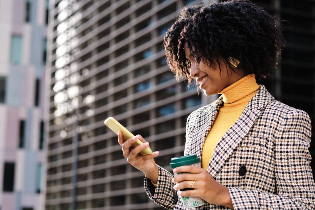 A businesswoman in a blazer looks at her phone while holding a cup of  coffee. 