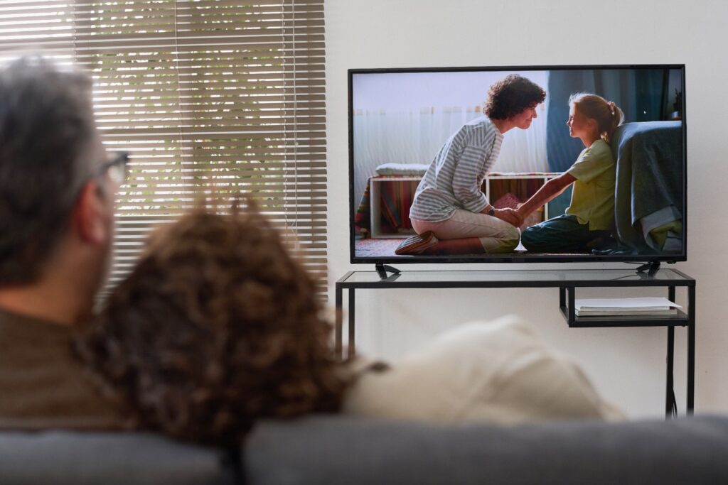 A view from behind as a couple sits on a couch watching television.